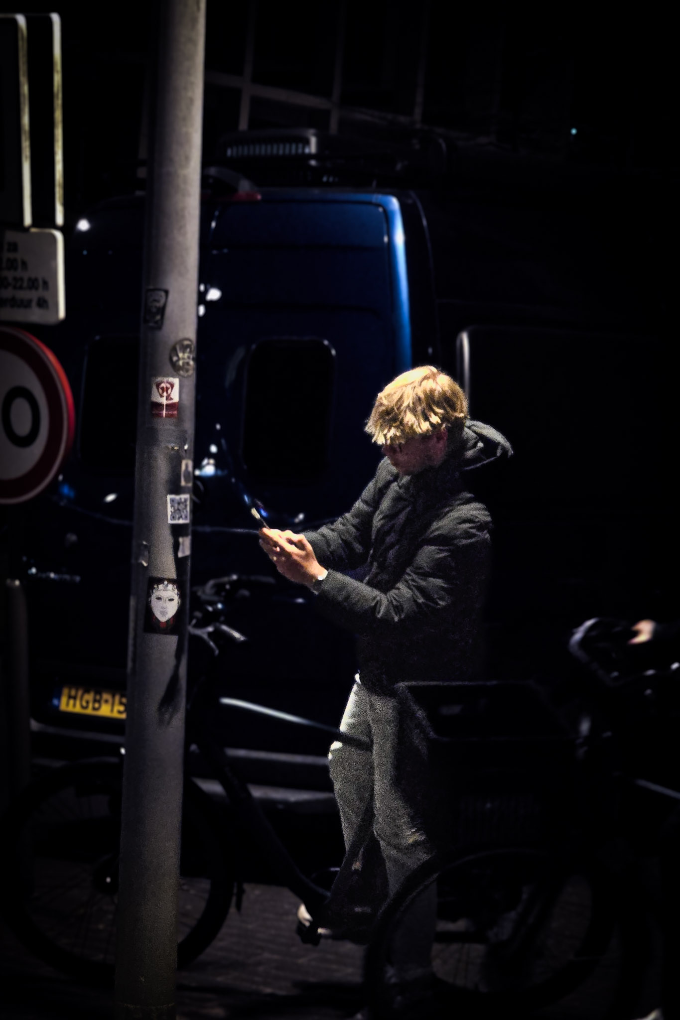 Jongen op een fiets kijkt op zijn telefoon in een donkere straat