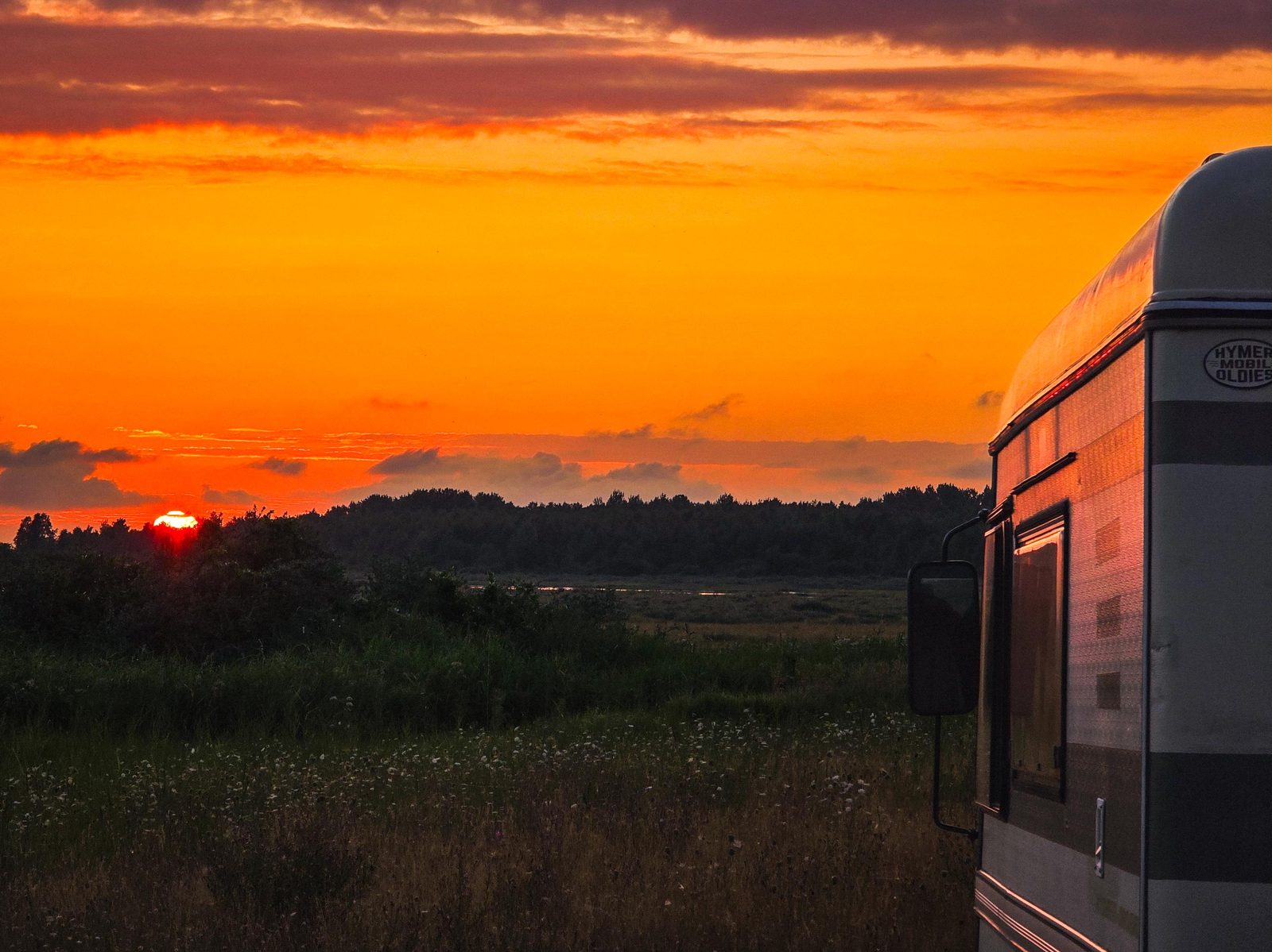 Camper in een veld bij een oranje zonsondergang
