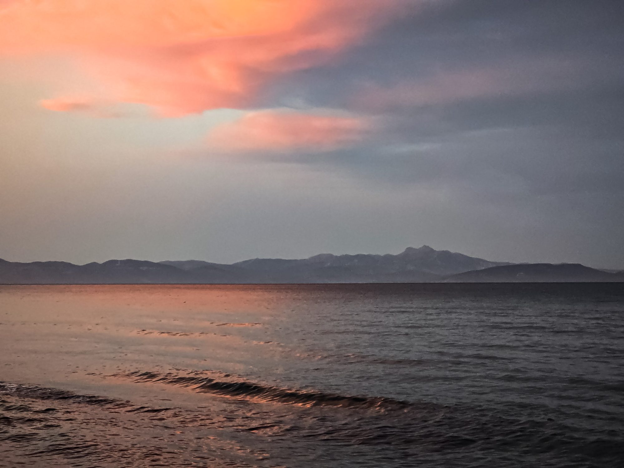 Zee met bergen aan de horizon bij zonsondergang